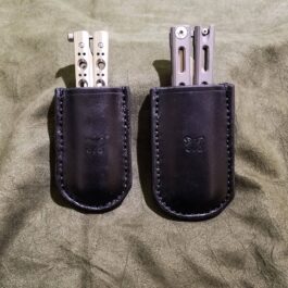 Two Benchmade Balisong knives in a Leather Sheath on a bed.