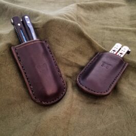 A couple of Leather Sheaths for Benchmade Balisong Knives sitting on top of a bed.