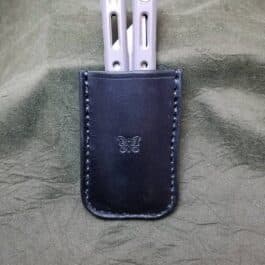 Three Benchmade Balisong knives in a leather sheath on a bed.