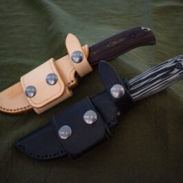 Two Leather Scout Sheaths For The Benchmade Saddle Mountain Skinner are laying on a green cloth.