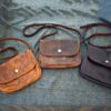 three leather bags sitting on top of a bed.