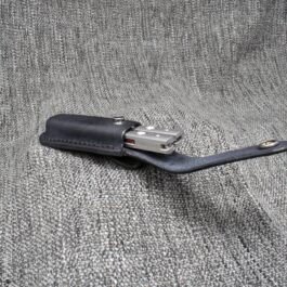 A black Molded Leather Belt Pouch for a Benchmade Balisong on gray fabric.