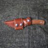 A handmade leather sheath for the Lionsteel M4 sitting on top of a gray cloth.