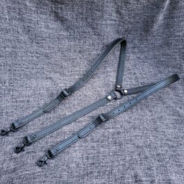 A pair of Upgraded Leather Suspenders laying on a gray cloth.