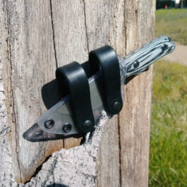 A Scout Style Kydex Sheath for Benchmade Hidden Canyon Hunter Style 2 stuck in a wooden post with a black handle.