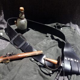 A Pirate Baldric Style 2, a bottle, and a knife laying on a cloth.