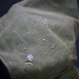 A close up of a Waxed Canvas Hooded Cloak with water drops on it.