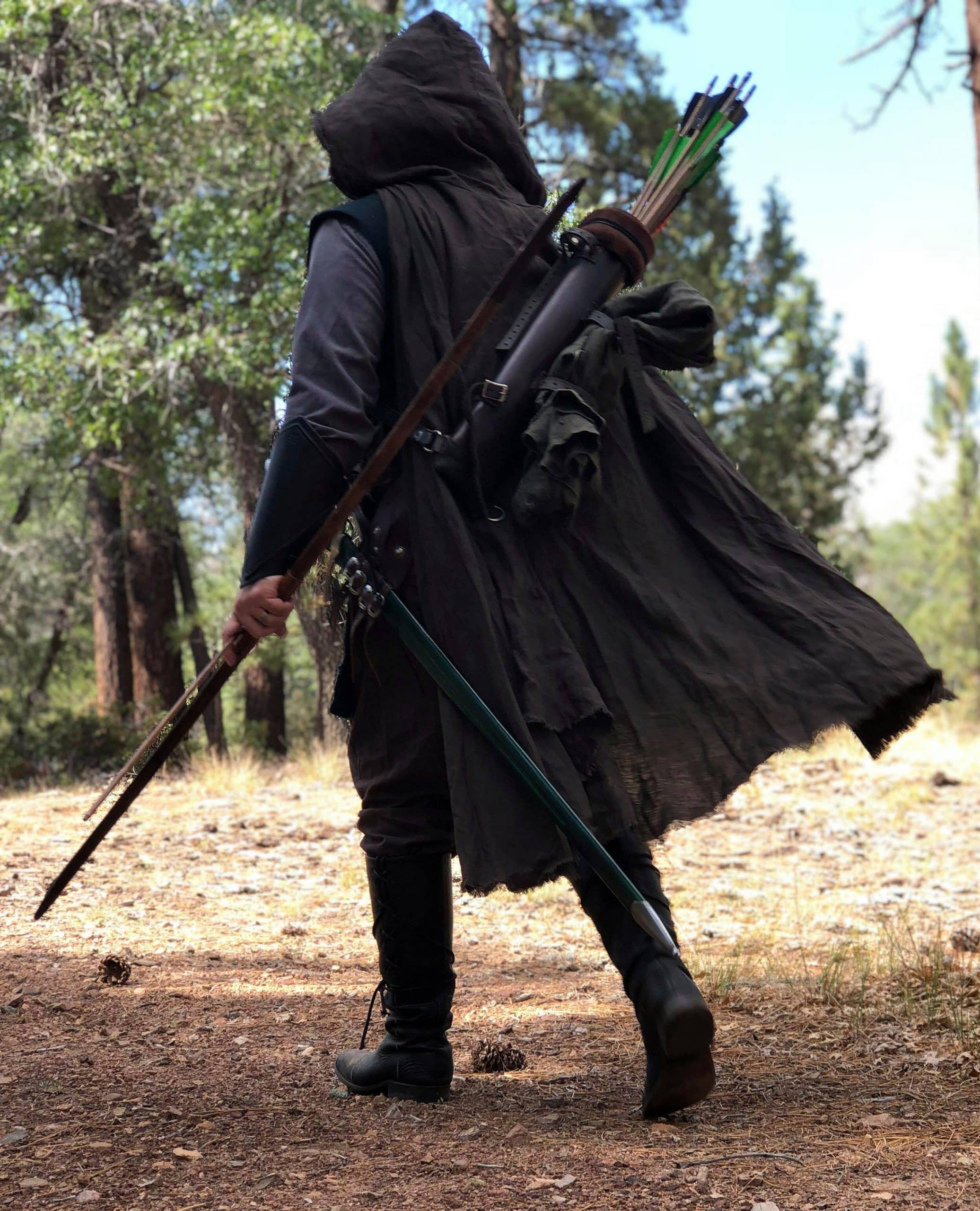 A man in a Linen Hooded Cloak holding two arrows.