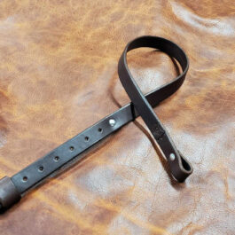 A black Simple Rifle Sling laid on a brown leather cloth - Grommet's Leathercraft - renaissance clothing - renaissance art clothing - renaissance era clothing - leathercraft supplies - leathercraft accessories - leathercraft store near me - quality leather craft