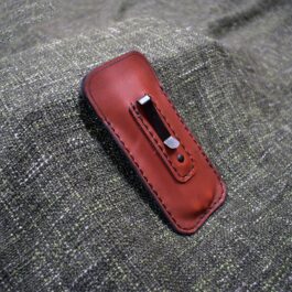 A red Leather Balisong Slip With Pocket Clip sitting on top of a couch.