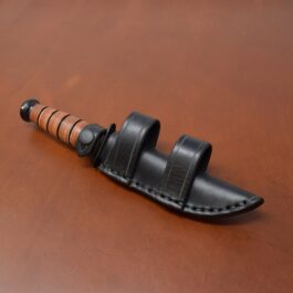 A black Leather Scout Sheath for the Short Ka Bar Fighting Knife on a brown table.