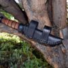 The Leather Scout Sheath for the Short Ka Bar Fighting Knife is stuck in a tree branch.