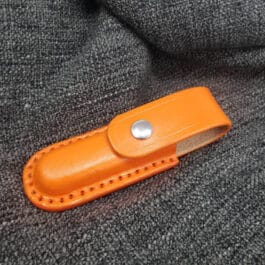 A molded leather belt pouch for a Benchmade Balisong resting on a gray sweater.