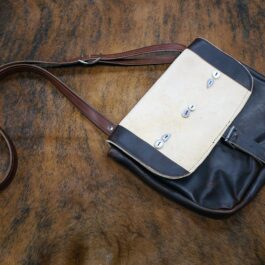 A black and white Arthur's Satchel sitting on top of a wooden table.