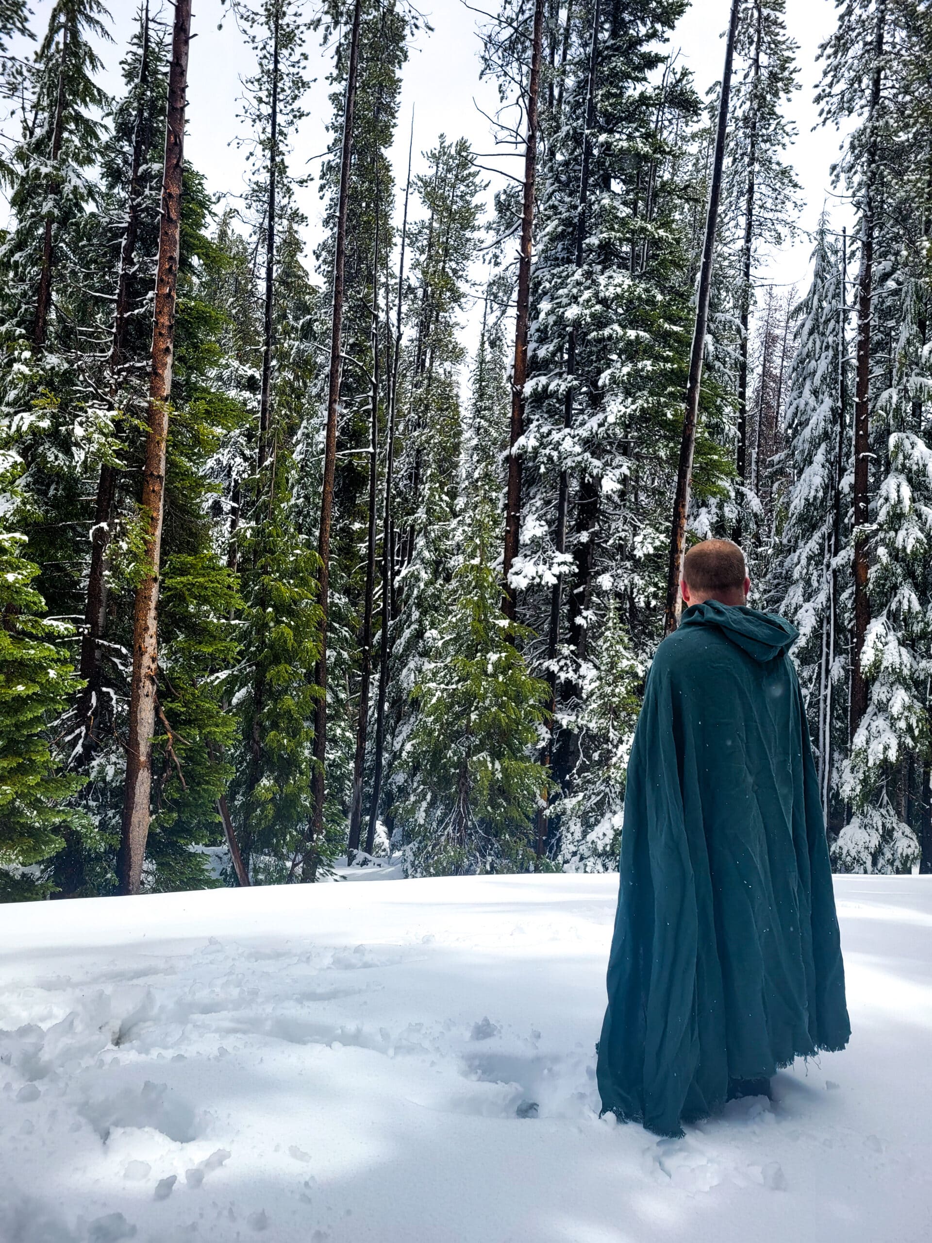 a man wearing a blue Linen Hooded Cloak on the snow - renaissance clothing - renaissance clothing men - renaissance clothing women - renaissance clothing near me - renaissance art clothing - renaissance era clothing - renaissance costume ideas