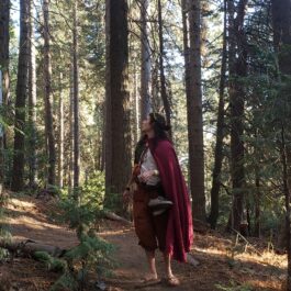 A woman in a Linen Hooded Cloak walking through a forest.