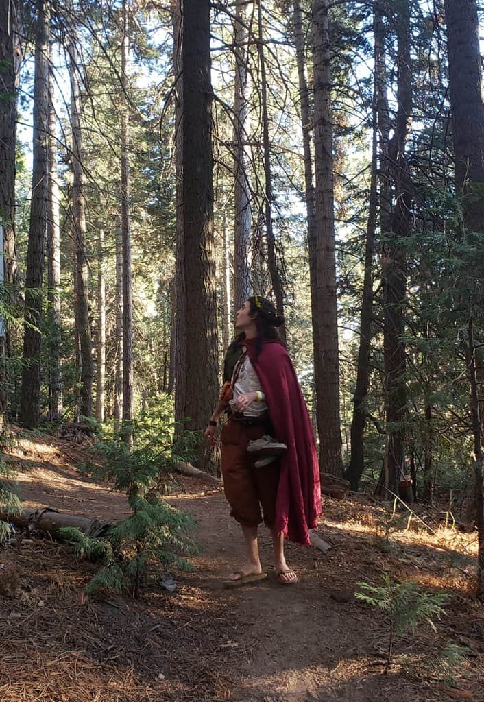 A woman in a Linen Hooded Cloak walking through a forest.