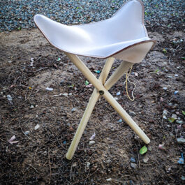 A Handmade Leather Camp Stool sitting on top of a dirt field.