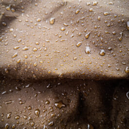 a close up of Waxed Canvas Hooded Cloak droplets on the sand.