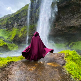 Boiled Wool Hooded Cloak in burgundy worn in front of a waterfall