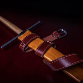 A Wood Core Scabbard for the Albion Liechtenauer with a leather strap on a table.