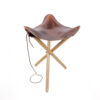 a brown leather camp stool with wooden legs