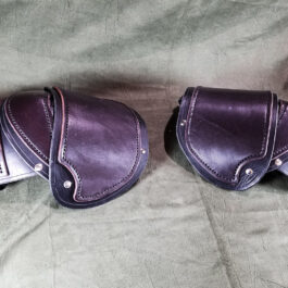 a pair of purple leather saddles sitting on a bed.
