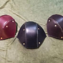 Three different colored Stitched Leather Back Of the Head Protections sitting on a bed.