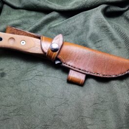A TOPS Fieldcraft Knife with a handmade leather sheath on a green cloth.