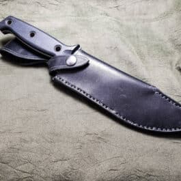 a knife with a leather sheath on a bed.
