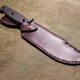 a knife with a leather sheath on a table.