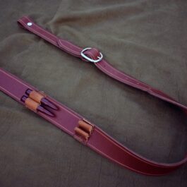 A burgundy Handmade Leather Rifle Sling with vertical ammo loops laid on a cloth - Grommet's Leathercraft - renaissance clothing - renaissance art clothing - renaissance era clothing - leathercraft supplies - leathercraft accessories - leathercraft store near me - quality leather craft