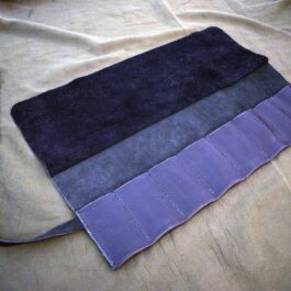 A Handmade Leather Knife/Tool Roll sitting on top of a bed.