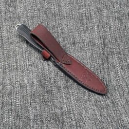 A handmade leather sheath for the Benchmade Fixed Infidel laying on top of a gray cloth.