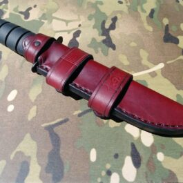 A Ka Bar Fighting Knife with a red Leather Scout Sheath on a camouflage background.