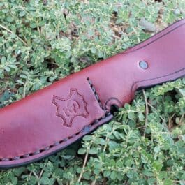 The Leather Sheath for the Benchmade Pardue Hunter laying on the ground in the grass.