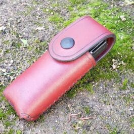 A red Handmade Leather Pouch sitting on top of a grass covered ground.