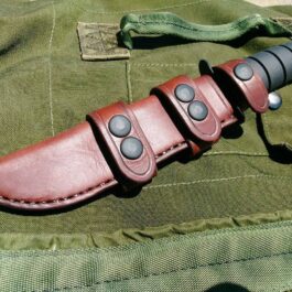 A Leather Scout Sheath for the Ka Bar Fighting Knife sitting on top of a green bag.