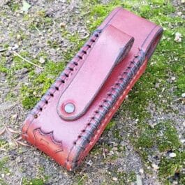 A red Handmade Leather Pouch sitting on top of a grass covered field.