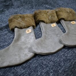 Three Handmade Reindeer Fur Christmas Stockings lined up on a bed.