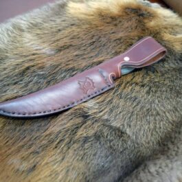 a brown leather knife laying on top of a fur covered chair.