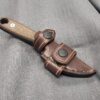 A Leather Scout Sheath for the Esee Izula on a gray cloth.