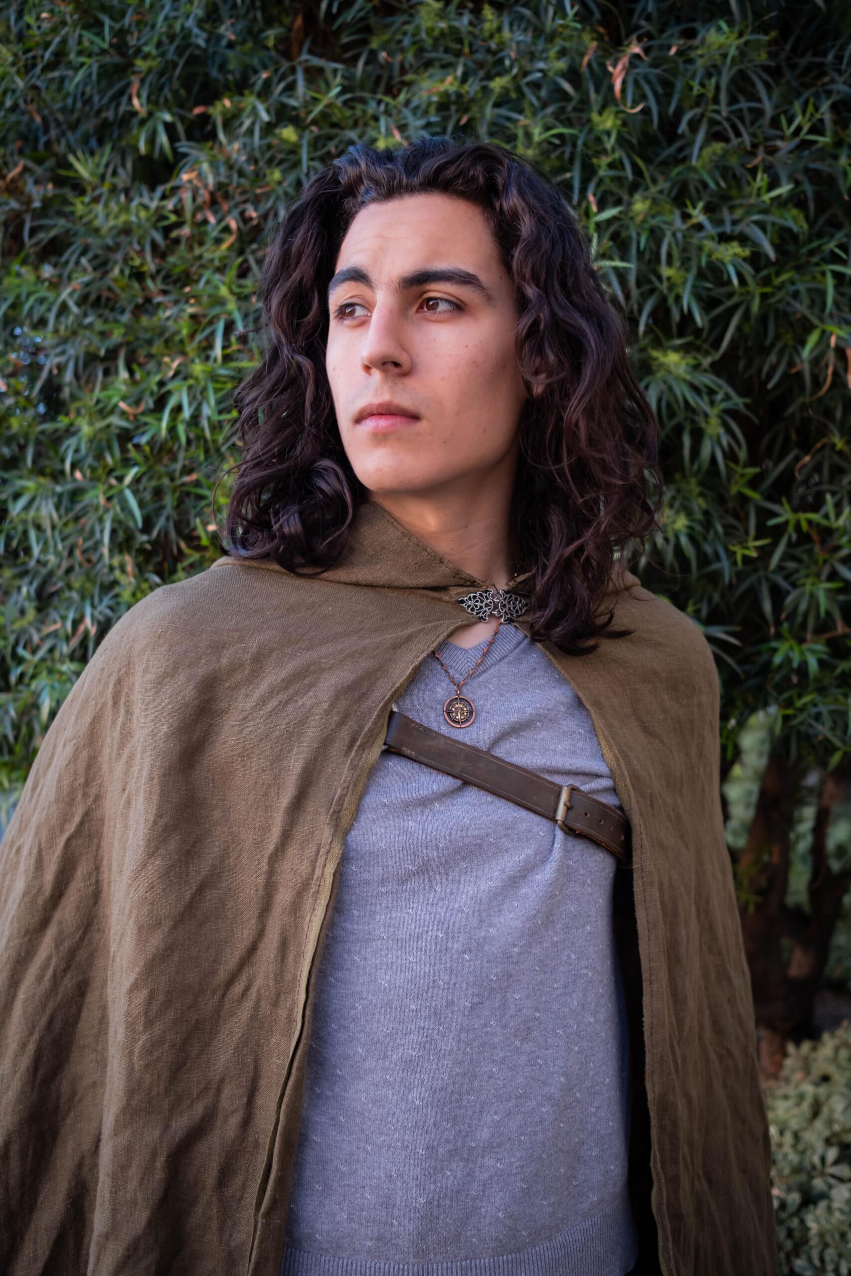 A man in a Linen Hooded Cloak standing in front of a bush.