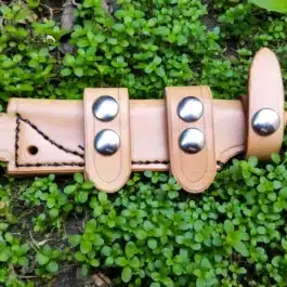a Scout Style Leather Sheath for the Benchmade Bushcrafter with three metal balls on it.