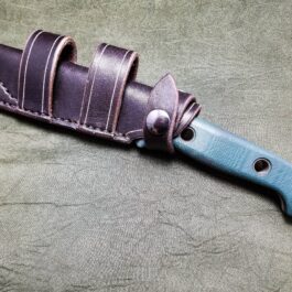 A Scout Style Leather Sheath for the Benchmade Bushcrafter knife on a table.