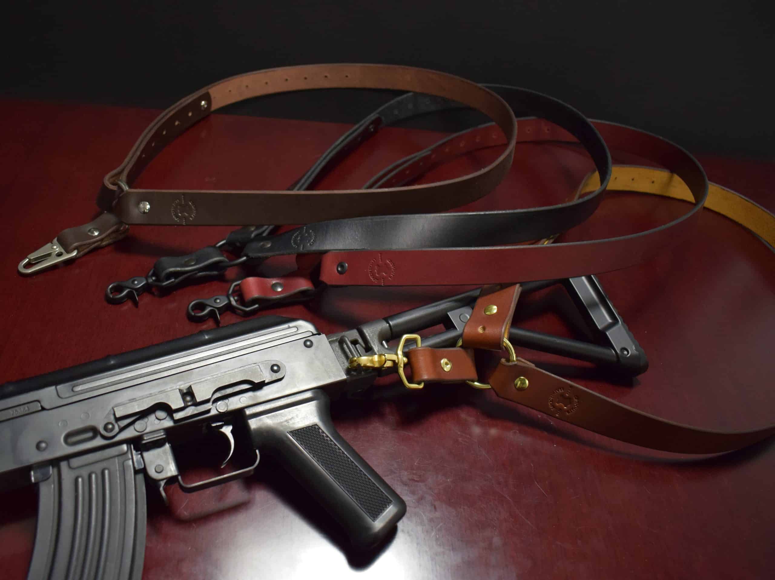 Four leather single point sling and a black gun laid on a wooden table - Grommet's Leathercraft - renaissance clothing - renaissance art clothing - renaissance era clothing - leathercraft supplies - leathercraft accessories - leathercraft store near me - quality leather craft