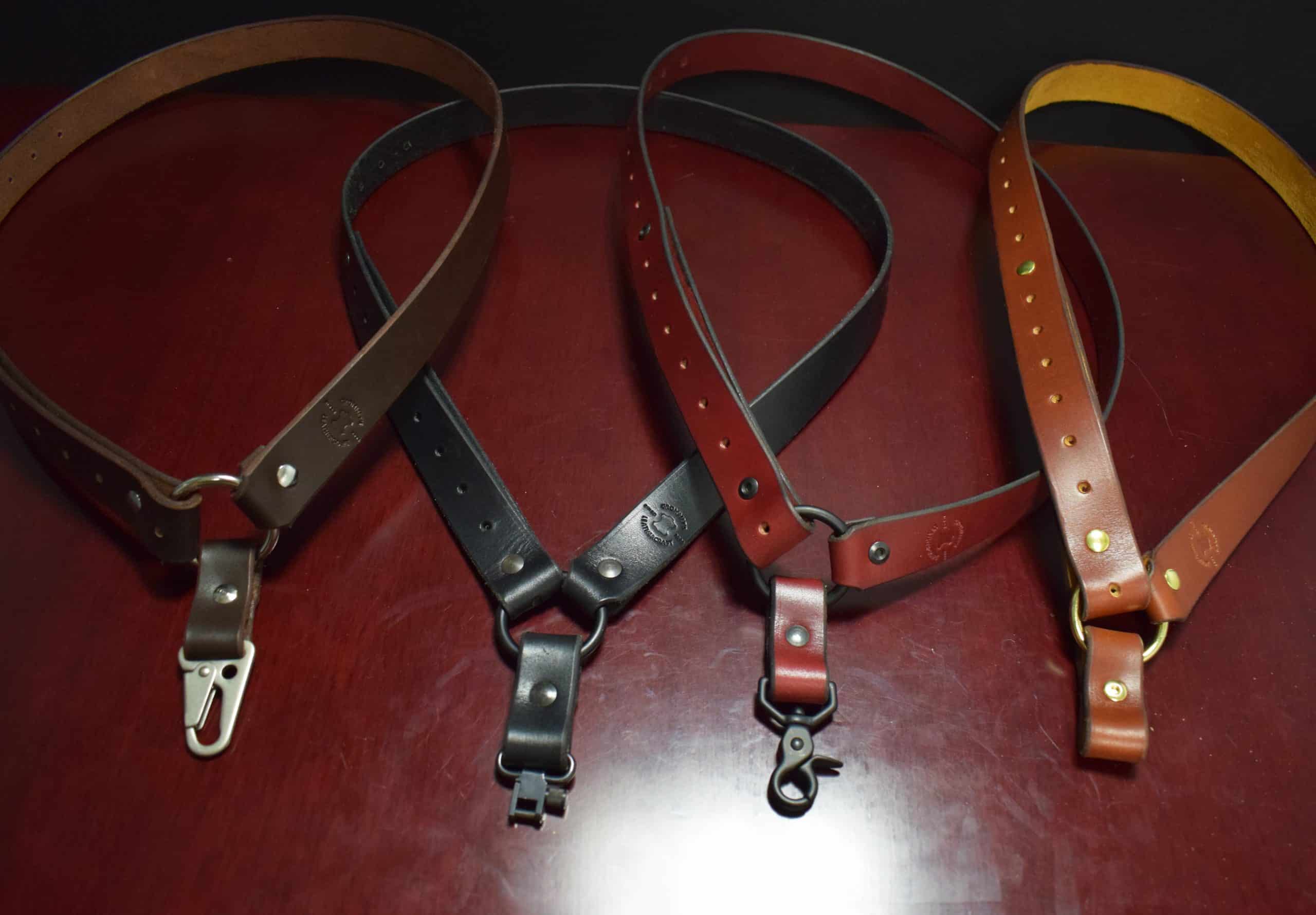 Two brown, one red, and one black leather single point sling laid on a wooden table - Grommet's Leathercraft - renaissance clothing - renaissance art clothing - renaissance era clothing - leathercraft supplies - leathercraft accessories - leathercraft store near me - quality leather craft