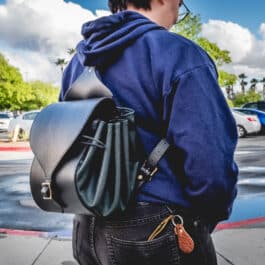 A man in a blue hoodie carrying a Leather Cinch Top Backpack.
