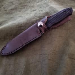 A Handmade Leather Sheath for the Benchmade Nimravus/Protagonist laying on top of a brown cloth.