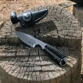 The Leather Scout Sheath for the White River Knives Backpacker/Caper is sitting on top of a tree stump.